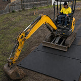 Mini excavator travelling on ground protection mats across a muddy worksite